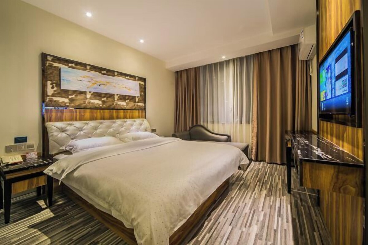 A hotel room with a large bed, a flat-screen TV, a wooden headboard, and a painting on the wall.