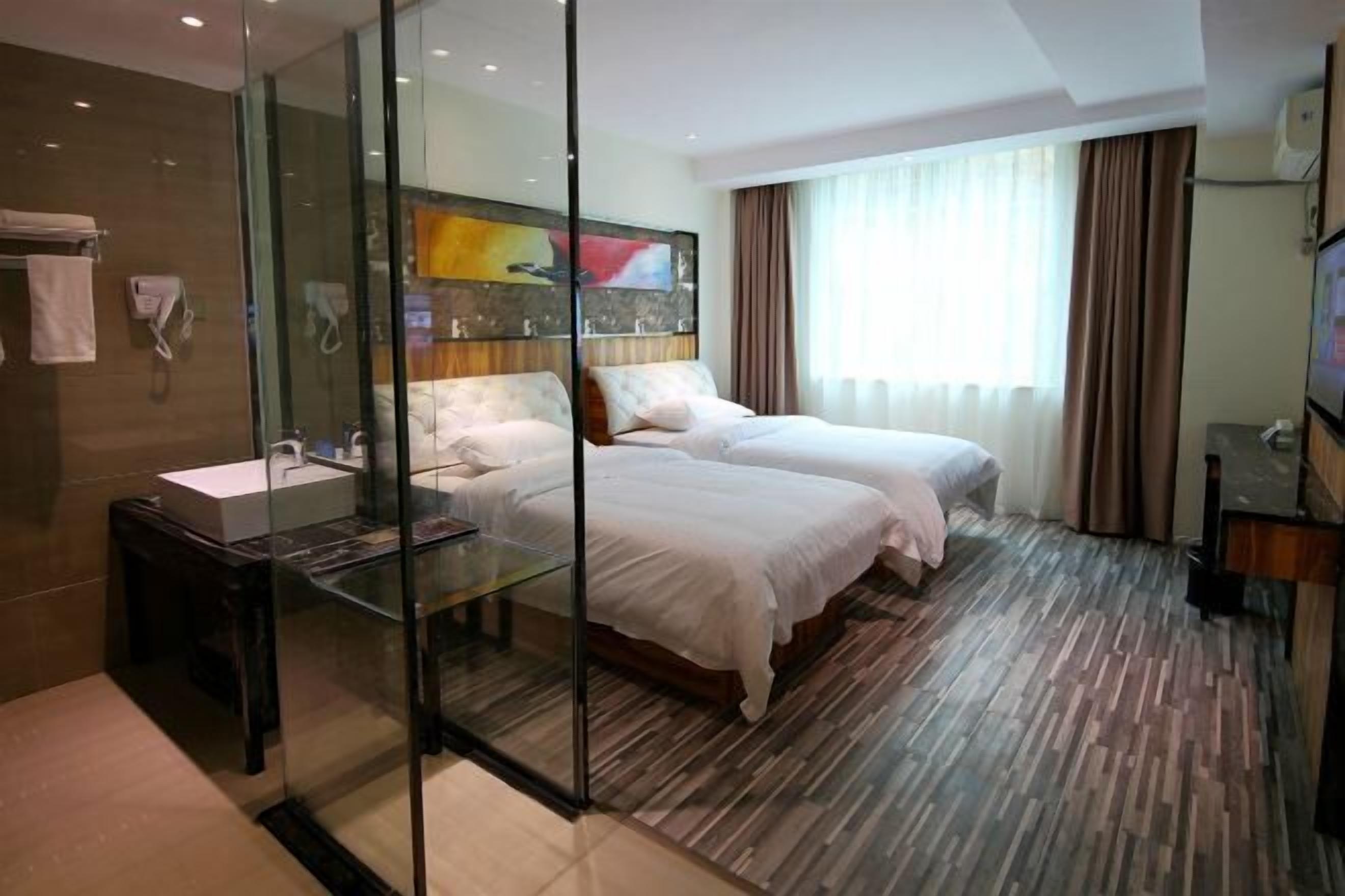 A hotel room with two beds, a glass partition, a sink, and a television.