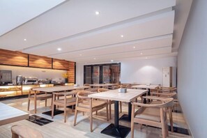 A modern dining area with wooden tables and chairs, a kitchen in the background, and a large window. - Nanning Unitour Hotel (Nanning)
