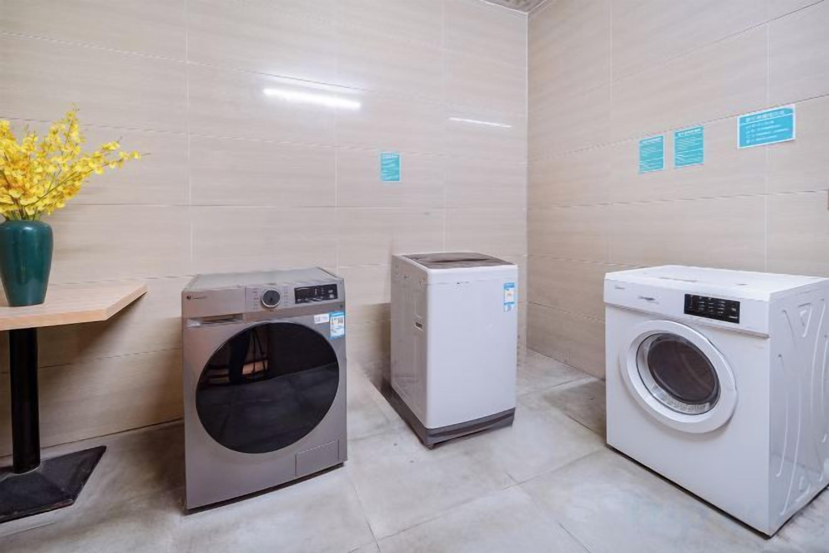 A laundry room with a washing machine, dryer, and a vase with yellow flowers on a table.