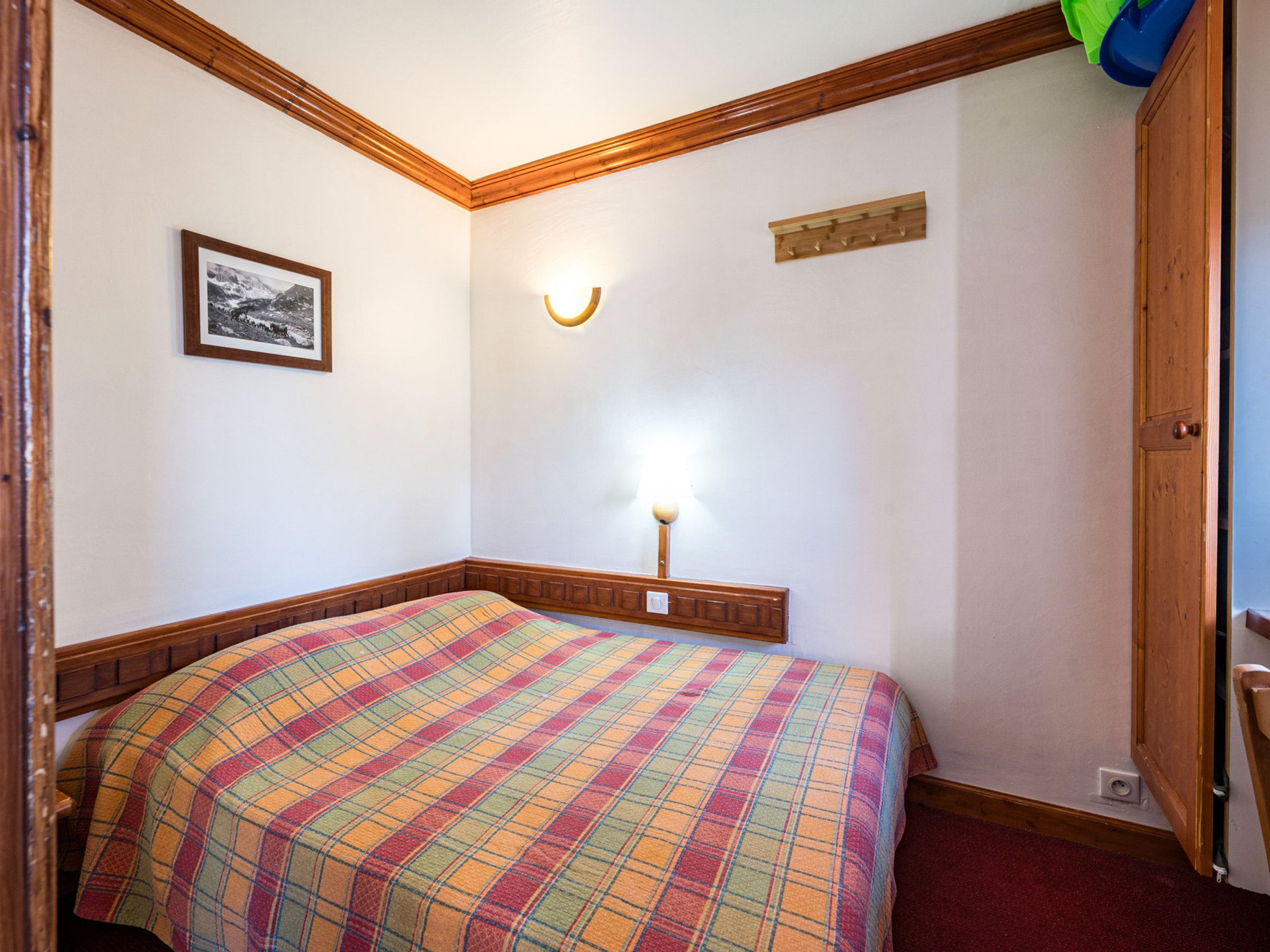 Une pièce comprenant un lit, un luminaire fixé au mur, un petit cadre et une porte en bois.