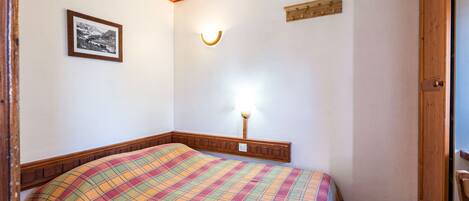 Quarto com cama, luminária na parede, pequeno porta-retrato e porta de madeira.