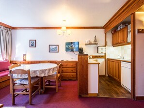 A cozy room with a dining table, chairs, a kitchen area with wooden cabinets, and a mounted sign.