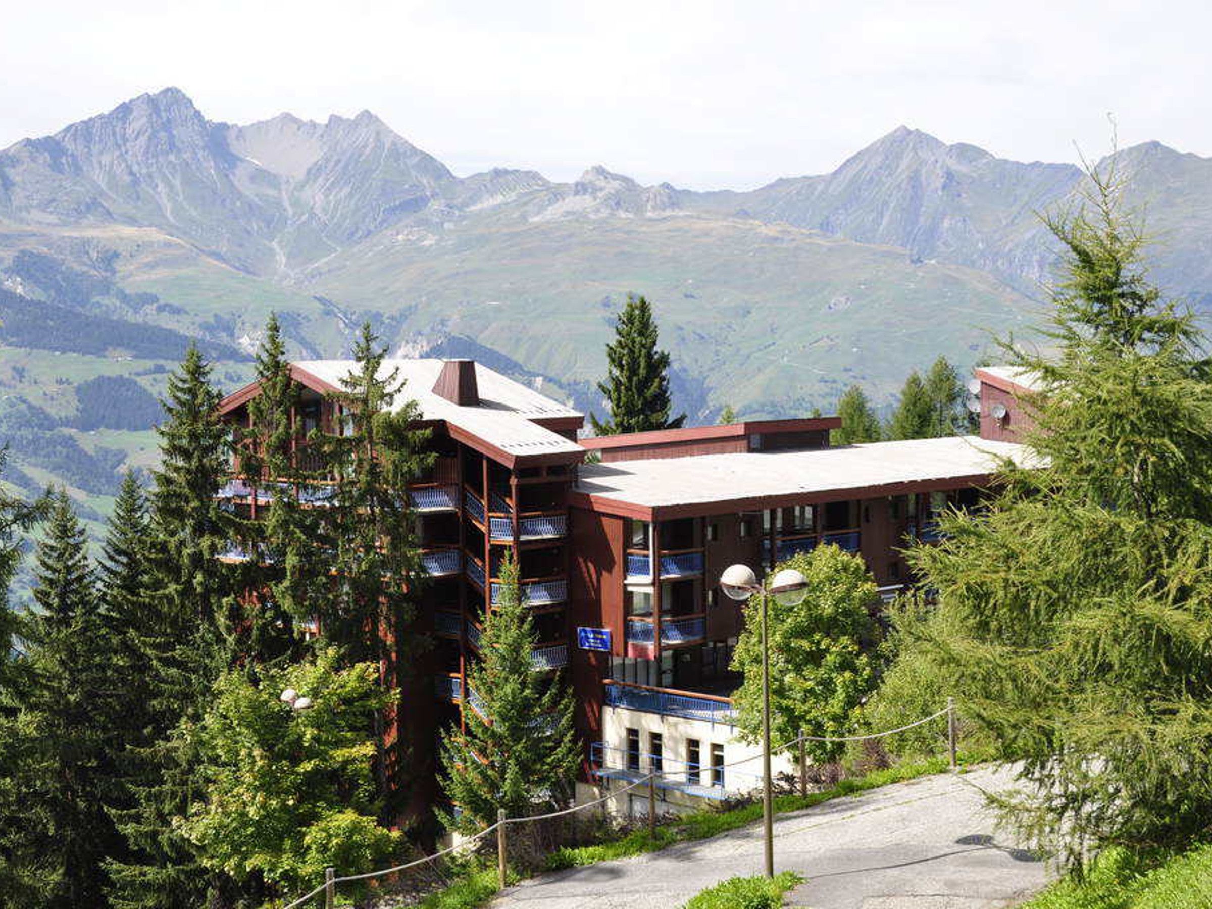 Un hotel de varios pisos con balcones, rodeado de montañas y árboles.