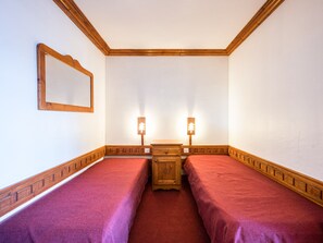 A room with two single beds, a wooden dresser, a mirror, and two wall-mounted lamps.