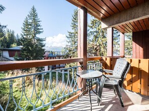 A balcony with a table and chairs, a wooden railing, and a view of trees and buildings.