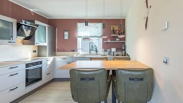 Una cocina moderna con armarios blancos, una mesa de comedor de madera y dos sillas verdes.