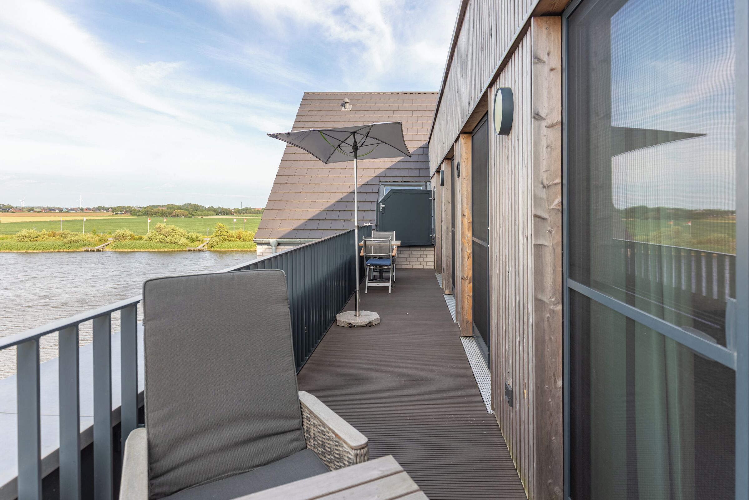 A balcony with a view of a river, a chair, and a table with an umbrella.
