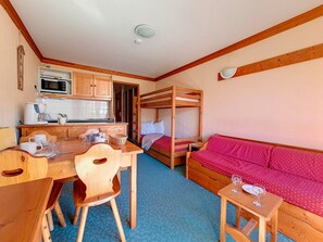 Una habitación compacta con literas, kitchenette, mesa de comedor con sillas y sofá.