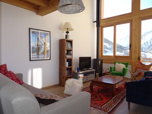 Una sala de estar con sofá, una mesa de centro, una estantería, televisor y un ventanal con vistas a la montaña.