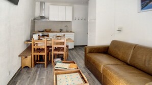 Kompakti oleskelutila, jossa on pieni keittiönurkkaus, ruokailualue puuhuonekaluilla sekä ruskea sohva.
