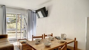 Ruokailutila, jossa on puinen pöytä, tuolit ja seinälle asennettu televisio.