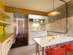Une cuisine compacte avec un coin repas, comprenant une table blanche, des chaises rouges et un luminaire suspendu.