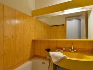 A wooden bathroom with a yellow sink, a mirror, and a bathtub.