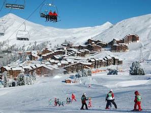 Uma estação de esqui com vários edifícios em estilo chalé, teleféricos e uma paisagem coberta de neve.