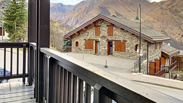 Ein Steinhaus mit Holzhörnern, einem Balkon und einem Berg im Hintergrund.