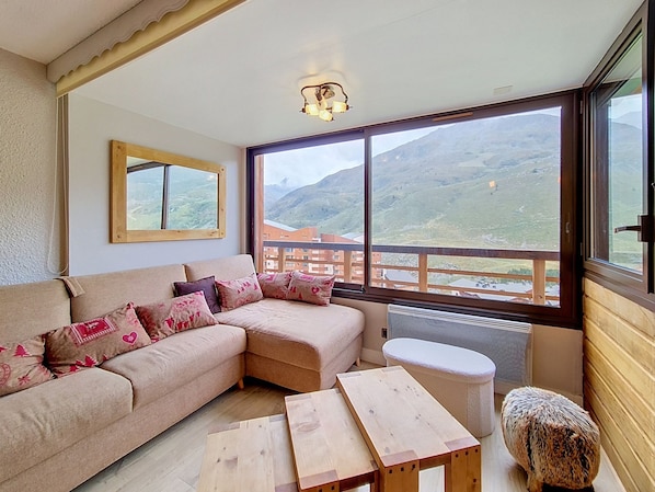 A cozy living room with a sofa, a small table, and a view of a mountainous landscape through large windows.