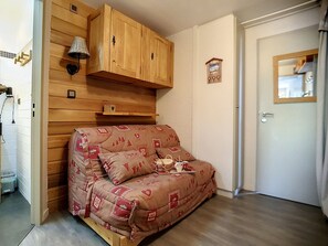 A cozy room with a wooden cabinet, a wall-mounted lamp, and a bed with a patterned cover. - Renovated, bright studio with ski-in/ski-out access (Les Menuires)