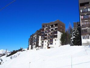 A multi-story hotel with balconies, a ski slope in the background, and snow-covered trees. - Renovated, bright studio with ski-in/ski-out access (Les Menuires)