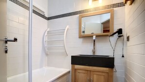 A bathroom with a bathtub, a shower, a sink with a mirror, and wooden cabinets.