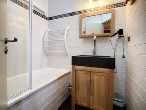 A bathroom with a bathtub, a shower, a sink with a mirror, and wooden cabinets.
