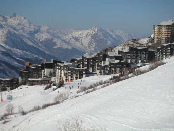 A ski resort with modern buildings, a ski slope, and snow-covered mountains in the background.