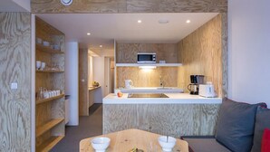 Cocina compacta con armarios de madera, microondas, cafetera y tostadora. Hay una mesa de comedor con un tazón de fruta y un tazón blanco.