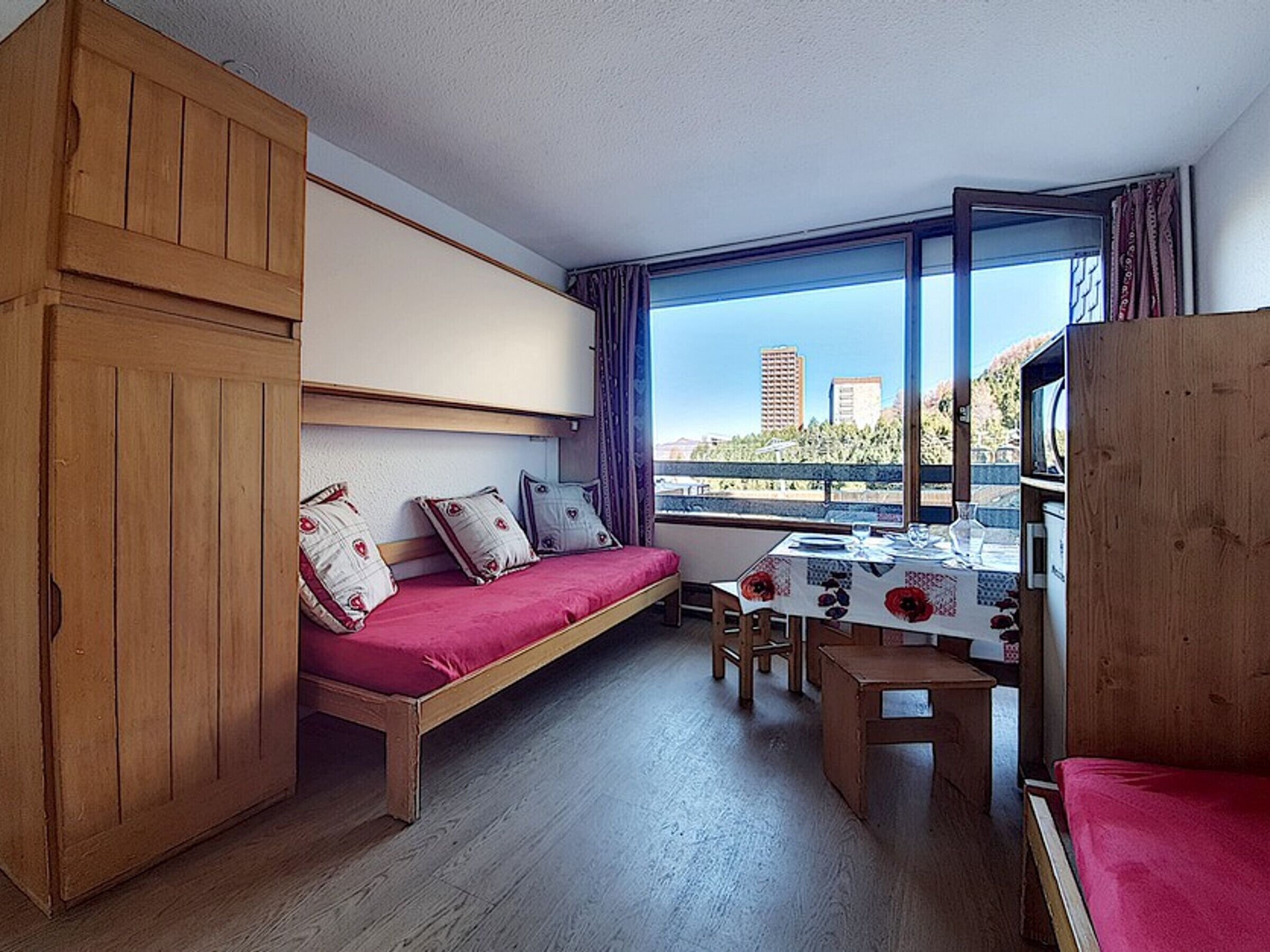 A compact room with a bed, a small table, and a window offering a city view.