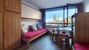 Una habitación pequeña con cama, una mesita y ventana con vistas a la ciudad.