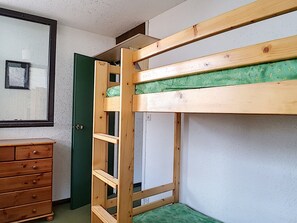 Una cama litera con colchón verde, un aparador de madera y una puerta.
