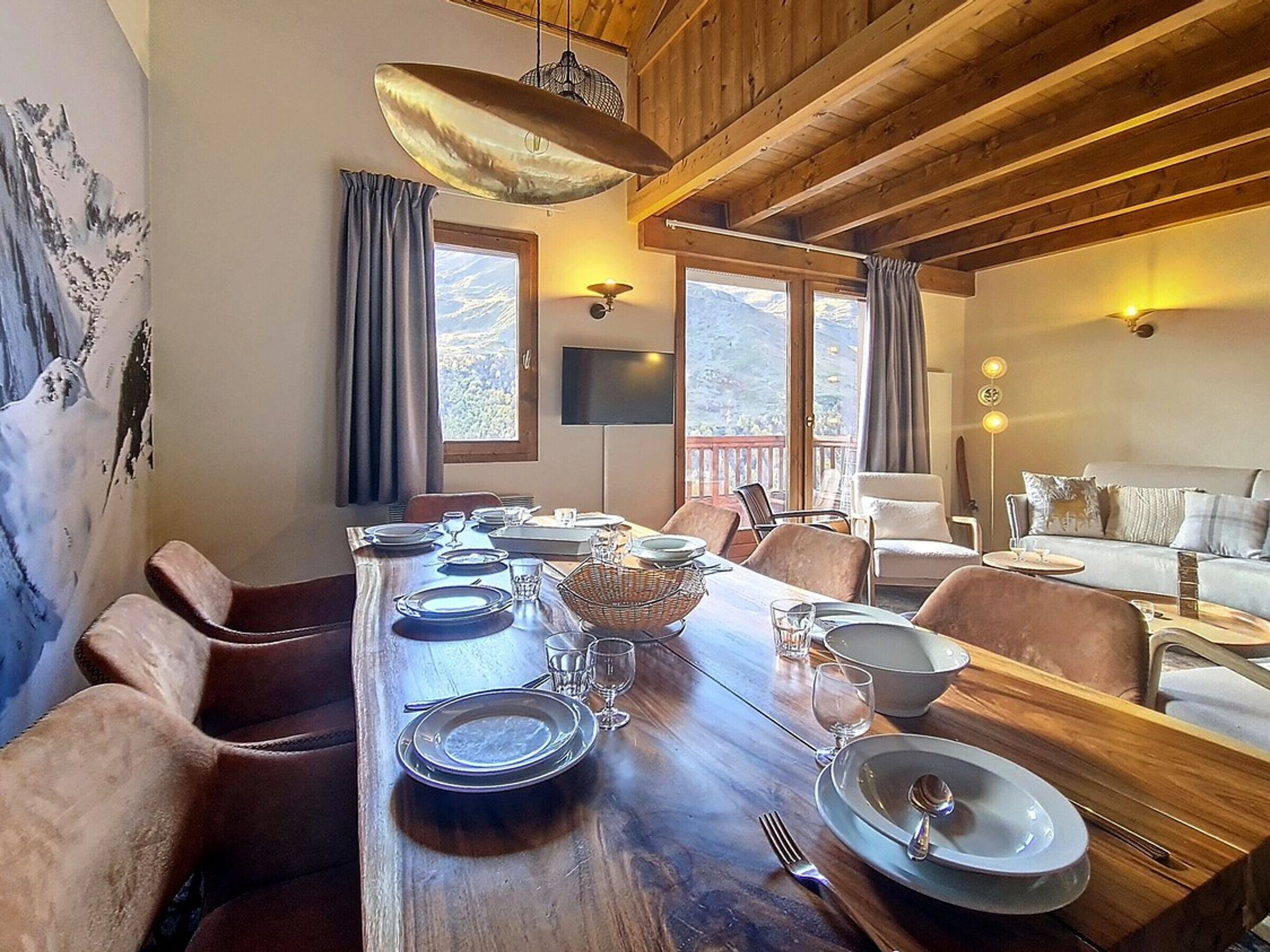 A dining area with a wooden table set for four, flanked by leather chairs, a large woven basket, and a sofa in the background.