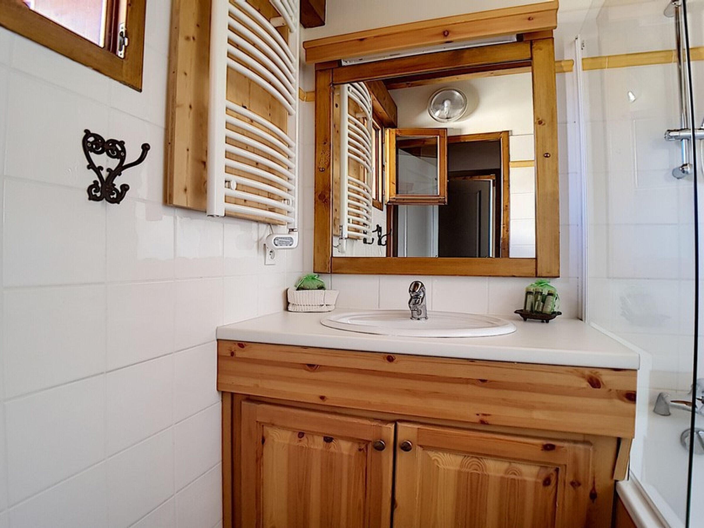 Une salle de bain avec un meuble-lavabo en bois, des carreaux blancs, un grand miroir et un espace douche.