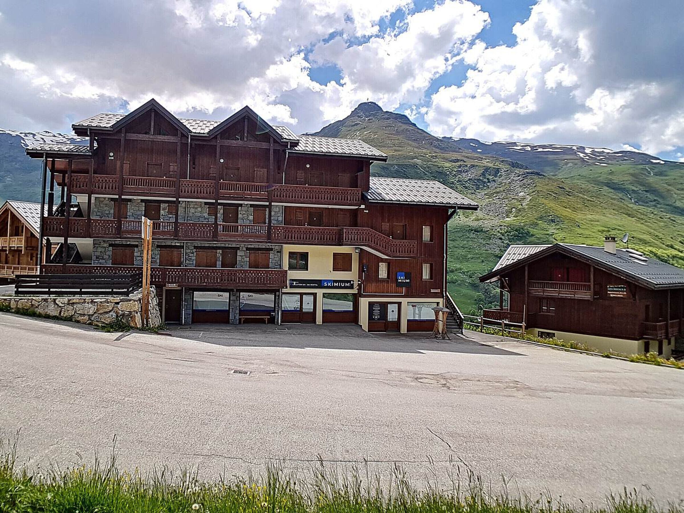 Un edificio de madera de varios pisos con balcones, señalización relacionada con el esqu í y un paisaje montañoso al fondo.