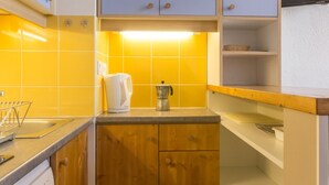 Une cuisine avec des carreaux de céramique jaunes, des meubles de rangement en bois, une machine à café et un lave-vaisselle.
