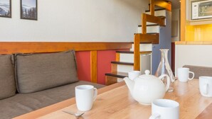 Un salon chaleureux avec une table en bois mise pour le thé, un canapé et un escalier doté d’une rampe en bois.