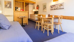 A cozy room with two beds, a dining table with chairs, a kitchen area, and artwork on the walls. - Bright studio · Ski-in/Ski-out · South balcony · Sleeps 4 (Les Arcs 2000)