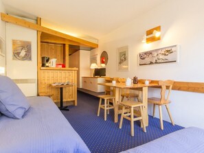 A cozy room with two beds, a dining table with chairs, a kitchen area, and artwork on the walls.