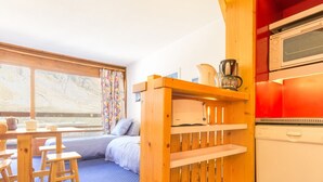 A cozy room with a bed, wooden furniture, a window with a view, and a kitchenette. - Bright studio · Ski-in/Ski-out · South balcony · Sleeps 4 (Les Arcs 2000)