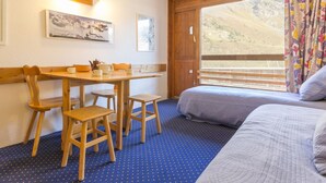 A room with a bed, a desk with chairs, a window with curtains, and artwork on the wall. - Bright studio · Ski-in/Ski-out · South balcony · Sleeps 4 (Les Arcs 2000)