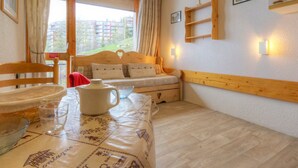 Une pièce chaleureuse avec un lit en bois, une table recouverte d’une nappe, une chaise et une fenêtre avec des rideaux.