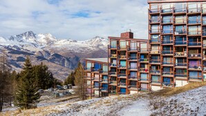 A multi-story building with balconies, set against a mountainous backdrop. - Cabin studio for 4, balcony, south facing, Les Arcs 1800 (Les Arcs 1800)