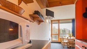 A kitchen with a microwave, a coffee machine, and a red oven. There is a dining area with a table and chairs, and a window with a view of trees. - Cabin studio for 4, balcony, south facing, Les Arcs 1800 (Les Arcs 1800)