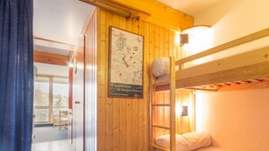 A wooden bunk bed room with a poster on the wall, a window, and a door leading to another room. - Cabin studio for 4, balcony, south facing, Les Arcs 1800 (Les Arcs 1800)