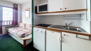 Una habitación pequeña con cama, kitchenette y ventana con cortinas.