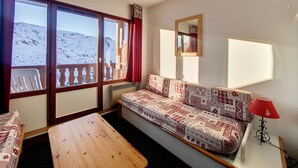 Una habitación acogedora con un sofá, una mesa y un ventanal con vistas a una montaña nevada.