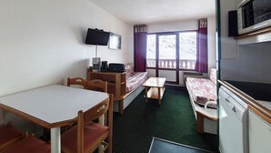 Habitación de hotel pequeña con cama, una mesita, escritorio, silla, televisor y microondas.