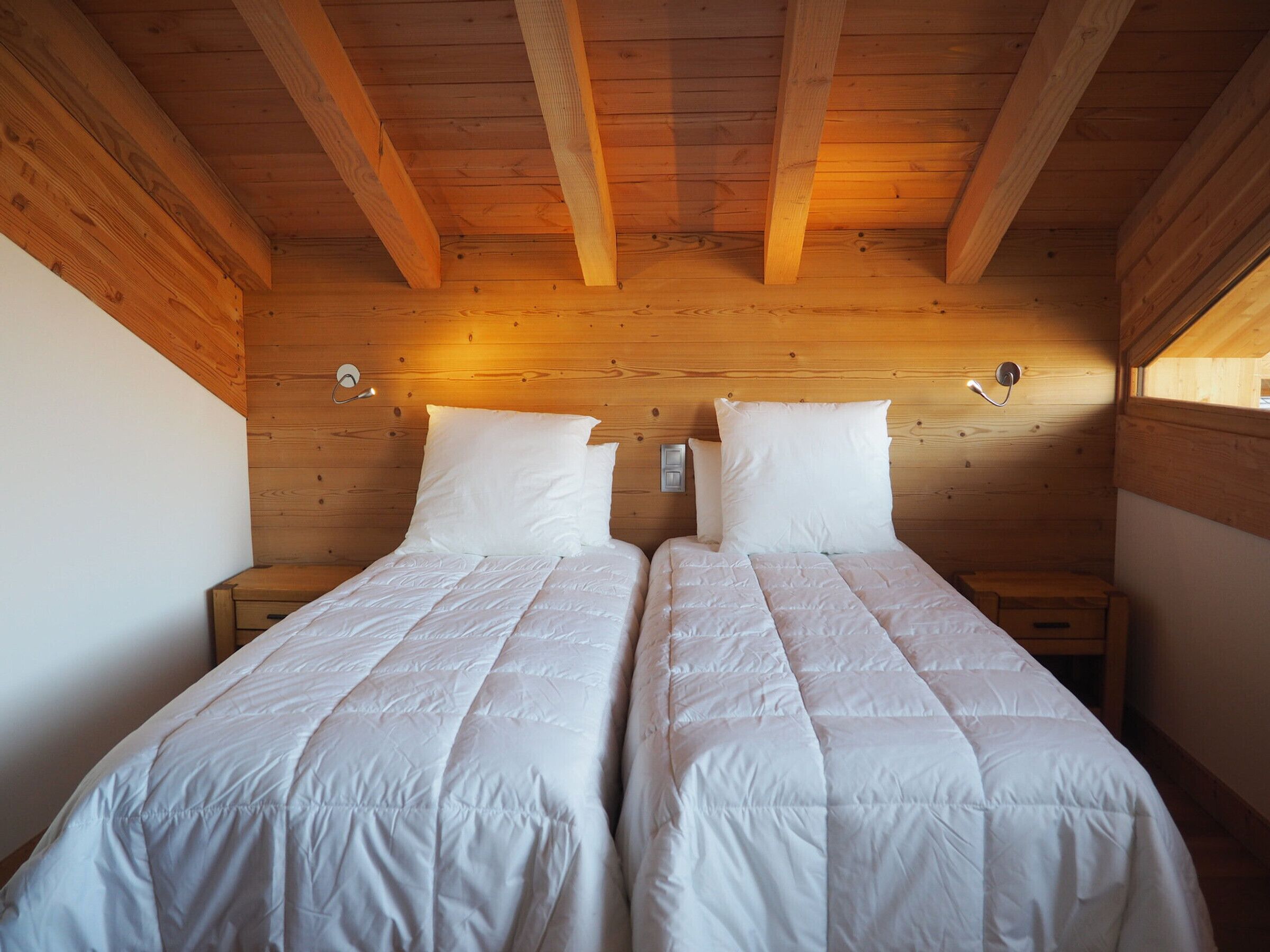 Een kamer met twee bedden, houten balken in het plafond en een klein raam.