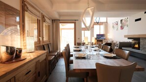 Ein moderner Essbereich mit einem Holztisch, gedeckt für sechs Personen, an dessen Seite Holzschränke und ein großes Fenster sind.