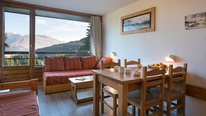 Une pièce chaleureuse avec un canapé en bois, une table à manger avec des chaises et une vue sur les montagnes grâce à de grandes fenêtres.