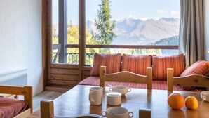 Une pièce chaleureuse avec une table en bois, des chaises et une vue sur les montagnes, visible à travers de grandes fenêtres.